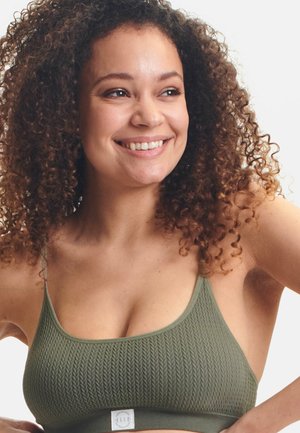 Bralette texturé vert olive avec de fines bretelles et un patch logo à la base, présentant un design côtelé et un matériau doux.
