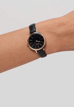 Black leather strap watch with a round, rose gold case and black face, featuring simple hour markers and a minimalist design.
