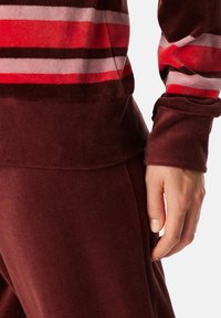 Samtoberteil mit kräftigen roten und pinken horizontalen Streifen, kombiniert mit einfarbigen burgunderfarbenen Hosen. Weicher Stoff und elastische Bündchen sind sichtbar.