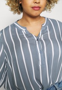 Blue and white striped blouse with a notch collar, button closure, and soft fabric texture. Features a relaxed fit and casual style.