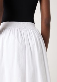 Jupe blanche légère, froncée avec une taille élastique, associée à un haut noir ajusté, mettant en valeur une texture lisse et un design simple.