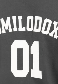 Camiseta gris con un gran texto en blanco que dice "SMILODOX" encima de "01". La tela parece suave con una textura lisa.
