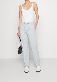 Světlomodré, zužující se kalhoty s elastickým pasem, bočními kapsami a hladkým povrchem. V kombinaci s bílými nazouvacími botami a malou černou taškou.