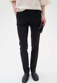 Černé tailored kalhoty s hladkou strukturou, vybavené bočními kapsami a slim-fit střihem, doplněné černými nazouvacími botami.