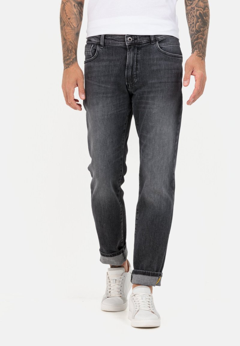 Schwarze Denim-Jeans mit geradem Schnitt, ausgewaschenem Finish, hochgekrempelten Säumen und Fronttaschen, getragen mit weißen Sneakers.