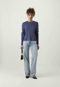 Suéter azul marinho, mangas longas, corte relaxado; jeans flare de lavagem clara; bolsa preta; saltos pretos de bico; texturas suaves.