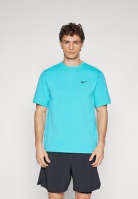 T-shirt de sport turquoise à manches courtes, col ras-du-cou, avec un petit logo Nike noir sur la poitrine. Porté avec un short sombre.