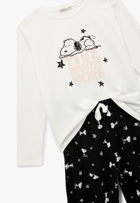 Hvid langærmet top med Snoopy grafik og teksten "FEM MINUTTER MERE". Sorte pyjamabukser med Snoopy og stjernemønster. Trækord.