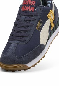 Zapatilla azul marino con parte superior de ante y textil, con una franja blanca, acentos dorados, talón a rayas y la marca "SUPER PUMA" en rojo.