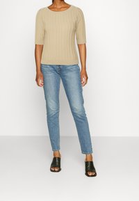 Top de punto acanalado beige con mangas cortas, combinado con jeans ajustados azul claro y zapatillas de punta abierta negras. Diseño minimalista en general.