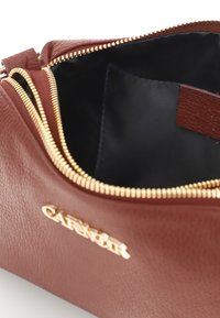 Brun läderväska med en texturerad yta, gulddragkedja och svart inredning. Har ett präglat logo på framsidan.