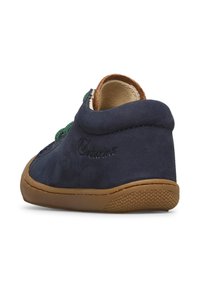 Scarpa basse in suede blu con lacci verdi, suola in gomma marrone, e dettaglio in rilievo del logo sul tallone. Texture morbida e forma curvata.