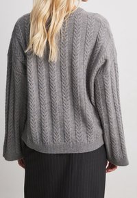 Grau gestrickter Pullover mit einer gerippten Textur und einem Zopf-Muster. Bietet einen lockeren Schnitt, weite Ärmel und einen abgerundeten Saum.