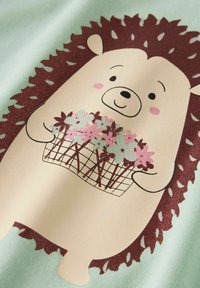 Cartoon egel met een mandje roze en lichtblauwe bloemen op een lichtblauwe stoffen achtergrond.