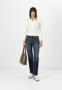 White long-sleeve henley top with button detail, dark blue straight-leg jeans, beige slip-on shoes, and a gray tote bag. Smooth texture.