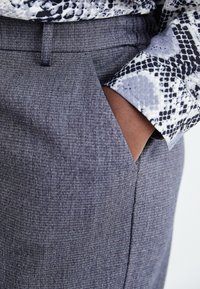 Grå texturerade byxor med slim fit och sidoficka, ihop med en mönstrad svartvit skjorta med ett ormmönster.