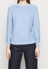 Ljusblått stickat tröja med rund halsringning, raglanärmar och ribbat nederkant och ärmslut. Har en texturerad tyg och en avslappnad passform.