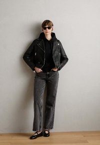 Black leather biker jacket over a black hoodie, paired with gray straight-leg jeans and black slip-on shoes. Smooth textures and minimalist design.