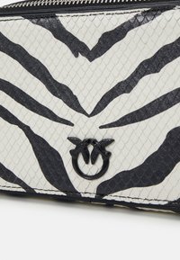 Cartera con patrón de cebra en material texturizado blanco y negro, con un logotipo que presenta dos aves y un cierre metálico.