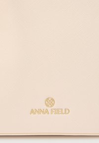 Επιφάνεια απαλού ροζ με υφή και ανάγλυφο λογότυπο 'ANNA FIELD' σε χρυσό. Διαθέτει σχεδιασμό με λείες άκρες.