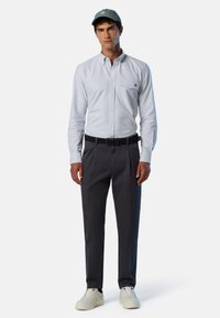 Camisa de rayas en blanco y azul, pantalones oscuros, gorra ajustada y zapatillas blancas, con un detalle de logo en el bolsillo de la camisa.