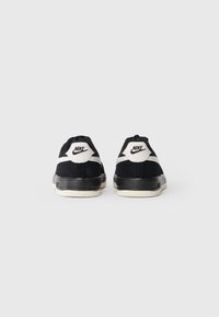 Crno-bijele Nike tenisice prikazane sa stražnje strane na jednostavnoj bijeloj pozadini, s Nike logom na petama.