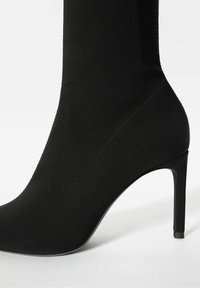 Czarne botki na wysokim obcasie z gładką, gładką cholewą, spiczastym noskiem i obcasem typu stiletto. Zawierają subtelne detale w przeszyciach.