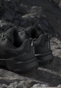 Scarpe da escursionismo Adidas Terrex nere su terreno roccioso, con talloni imbottiti, linguette per tirare e suole spesse e robuste.