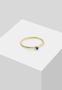 Anello d'oro con una fascia sottile e una piccola pietra blu, caratterizzato da un design minimalista e una texture liscia.