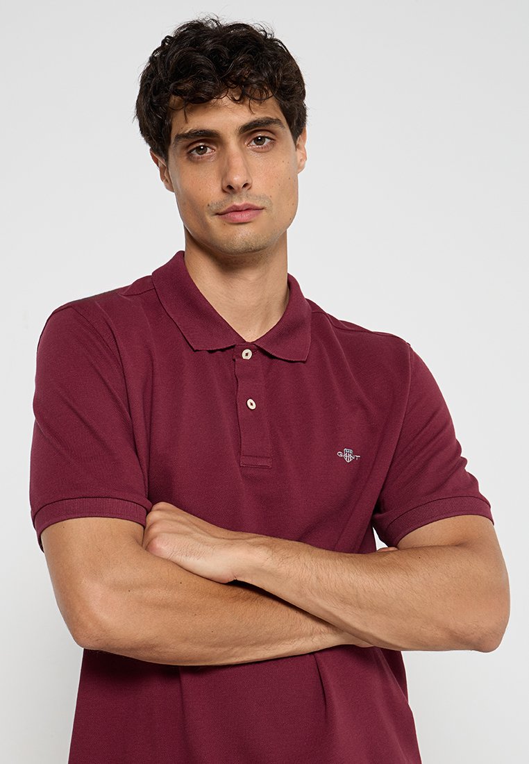 Polo bordeaux avec un col, une patte de boutonnage à deux boutons et des manches côtelées. Présente un petit logo sur la poitrine gauche. Matière en mélange de coton.