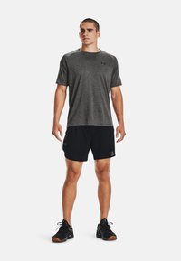 Grå kortermet treningstrøye med svarte detaljer, kombinert med svarte shorts og sorte treningssko med oransje såler.