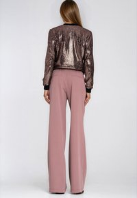 Kurtka bomberka z cekinami w kolorze różowego złota z czarnym prążkowanym kołnierzem i mankietami; w zestawie z jasnoróżowymi, szerokimi spodniami z tylnymi kieszeniami.