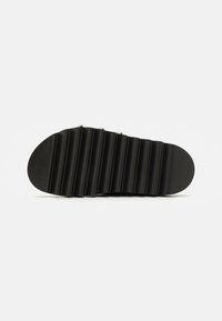 Semelle de chaussure en caoutchouc noir avec une texture striée et un bout arrondi, dotée de clous métalliques le long du bord supérieur pour un aspect supplémentaire.