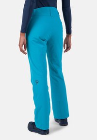 Türkise Skihosen mit hohem Bund, weichem Stoff und seitlichem Logo. Stilvoll gestaltet für Funktionalität und Komfort bei Winteraktivitäten.