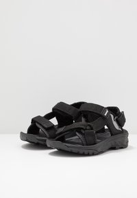 Black sport sandals with textured fabric straps, adjustable buckles, and a rugged rubber sole. Lightweight design for outdoor activities.