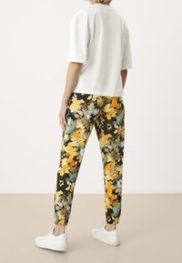 Biała koszulka z krótkim rękawem w połączeniu z czarnymi spodniami dresowymi ozdobionymi kolorowym kwiatowym wzorem w żółtym, zielonym i pomarańczowym kolorze, z elastycznymi mankietami.