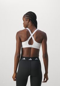 Vit sportbh med en crossover baksidesdetalj och ett nyckelhålsutskärning. Bärs tillsammans med svarta tights som har en vit logotyp vid midjan.