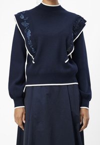 Marineblauwe trui met witte afwerking, textuurdetails op de schouders en lange mouwen. Gemaakt van een zacht materiaal, met een aansluitende taille.