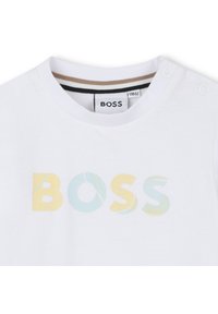 Hvit bomull T-skjorte med "BOSS"-logo i pastellfarger av gul og blå, med stripete halslinje og trykknapper på skulderen.