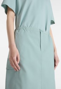 Light blue, short-sleeved garment with an elastic waist, featuring a button closure and side pockets, made of smooth, lightweight fabric.