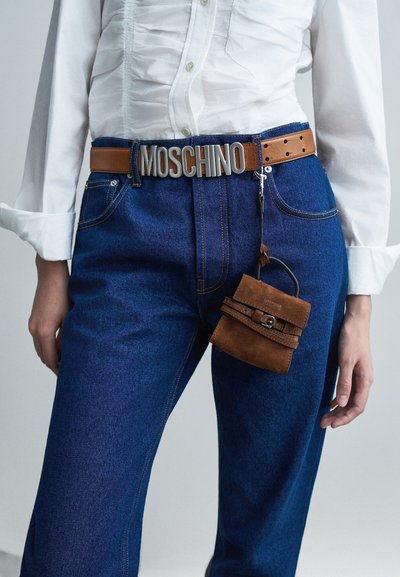 Cintura in pelle marrone con logo "MOSCHINO", abbinata a jeans in denim blu. Piccola borsa in suede marrone è attaccata alla cintura con una tracolla.
