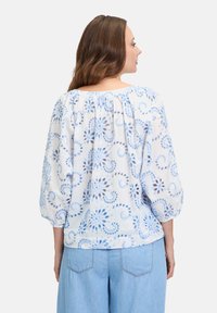Witte blouse met blauw bloemenpatroon, pofmouwen, geplooide halslijn en lichtgewicht stof. Gecombineerd met lichtblauwe denim broek.