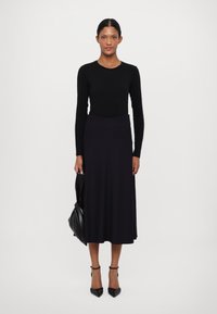 Musta pitkähihainen paita pyöreällä kaula-aukolla, yhdistettynä tumman sävyiseen, väljään midi-hameeseen. Malli pitää mustaa käsilaukkua ja käyttää mustia korkokenkiä.