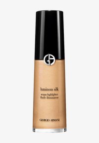 Illuminateur liquide Luminous Silk de Giorgio Armani dans une bouteille transparente haute et élancée avec un capuchon noir et un logo argenté, présentant un liquide doré scintillant.