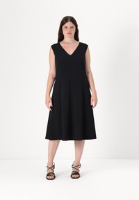 Černé áčkové šaty s výstřihem do V a bez rukávů, vyrobené z měkké látky. Kombinované s černými sandály na řemínky. Jednoduchý a elegantní vzhled.