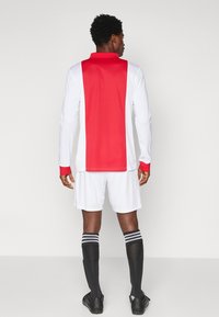 Gara ilgu piedurkņu futbols krekls sarkanā un baltā krāsā, ar vienkrāsainu sarkanu muguru un sarkaniem aproces. Valkāts ar baltām šortiem un melnām zeķēm.