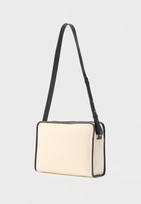 Beige skuldertaske i lærred med sort læderkant. Rektangulær form, justerbar rem og struktureret design. Ingen synlige logoer eller mønstre.