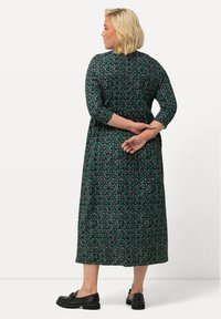 Vestido maxi negro con estampado floral verde. Presenta mangas tres cuartos, corte holgado y longitud a mitad de pantorrilla. Combinado con calzado negro.