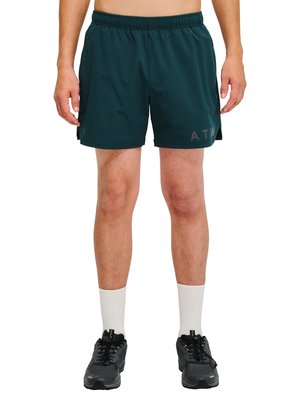 Mężczyzna ubrany w ciemnozielone krótkie spodenki sportowe, białe skarpetki i czarne buty do biegania, stojący z nogami lekko rozstawionymi na białym tle.