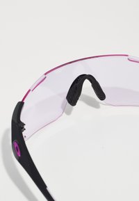 Sportsonnenbrille mit schwarzem Rahmen, pinken Akzenten und transparenten Linsen. Sie verfügt über ein gebogenes Design und gummierte Nasenpads für zusätzlichen Komfort.